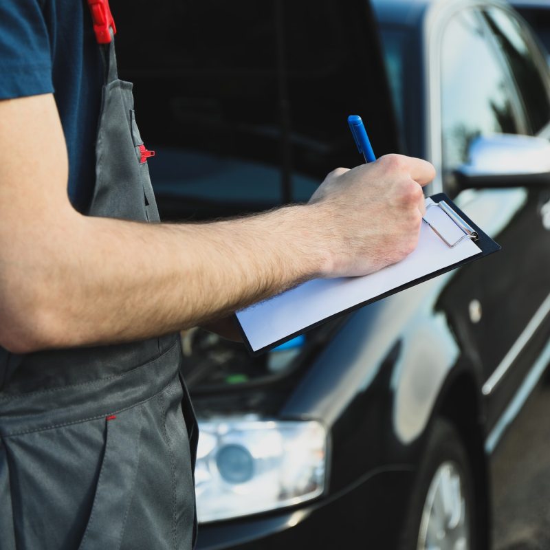 a-man-in-overalls-writes-to-a-clipboard-mechanic-car-inspection.jpg